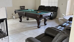 Un salon avec une table de billard, des canapés en cuir et un tableau encadré au mur.