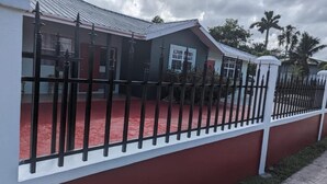 A house with a red exterior, a black metal fence, and a red carpeted area in front.