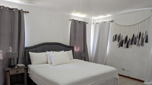 A bedroom with a large bed, a bedside table with a lamp, and curtains on the windows.