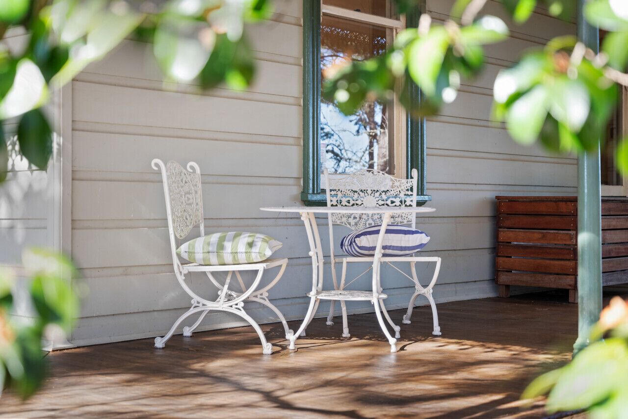 A white metal table and chairs with patterned cushions on a porch with wooden flooring.