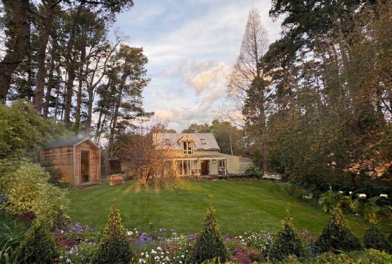 A house with a well-maintained lawn and garden, surrounded by tall trees.