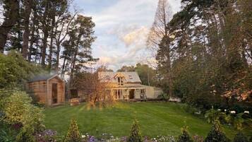 A house with a well-maintained lawn and garden, surrounded by tall trees.