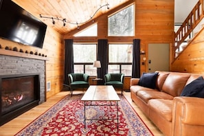Ein gemütliches Holzblockhaus-Interieur mit Kamin, Ledersofa und großem Wandfernseher.