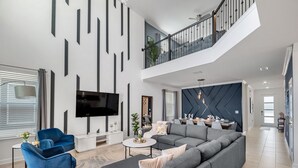Ein modernes Wohnzimmer mit einem grauen Ecksofa, einem blauen Sessel und einem flachbildfernseher, der an der Wand befestigt ist.