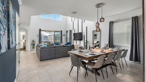 Ein modernes Wohnzimmer mit Essbereich, großen Fenstern und einem grauen Sofa.