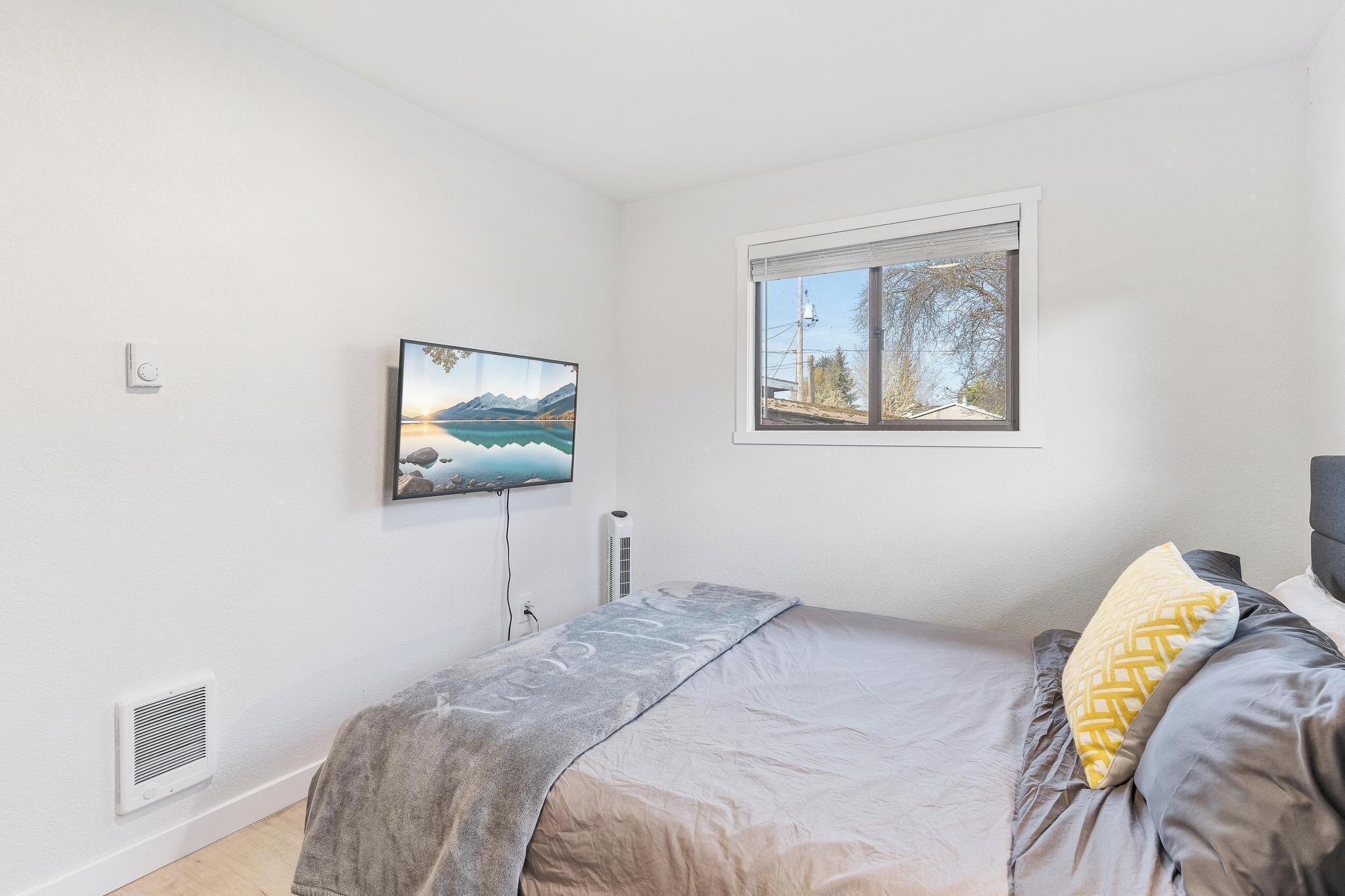 Ein Schlafzimmer mit einem Bett, einem Fenster mit Blick auf Bäume, einem an der Wand montierten Fernseher und einem Wandheizkörper.
