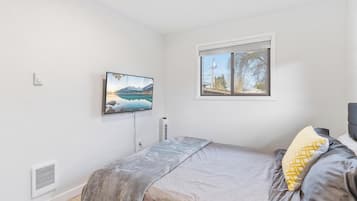 Ein Schlafzimmer mit einem Bett, einem Fenster mit Blick auf Bäume, einem an der Wand montierten Fernseher und einem Wandheizkörper.