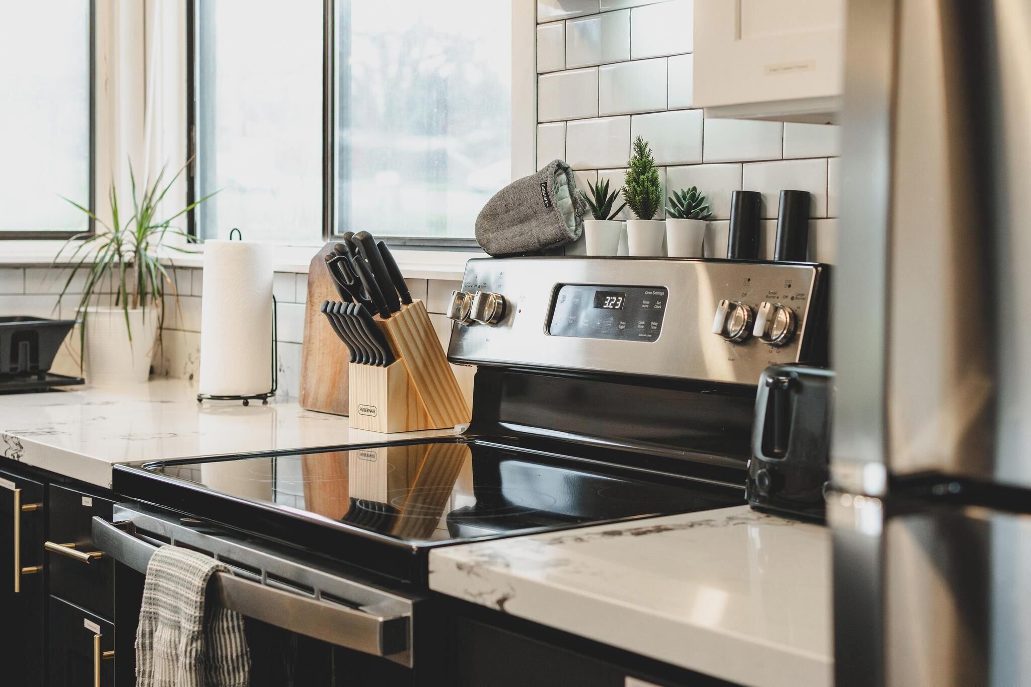 A modern kitchen with stainless steel appliances, a marble countertop, and a window with plants.