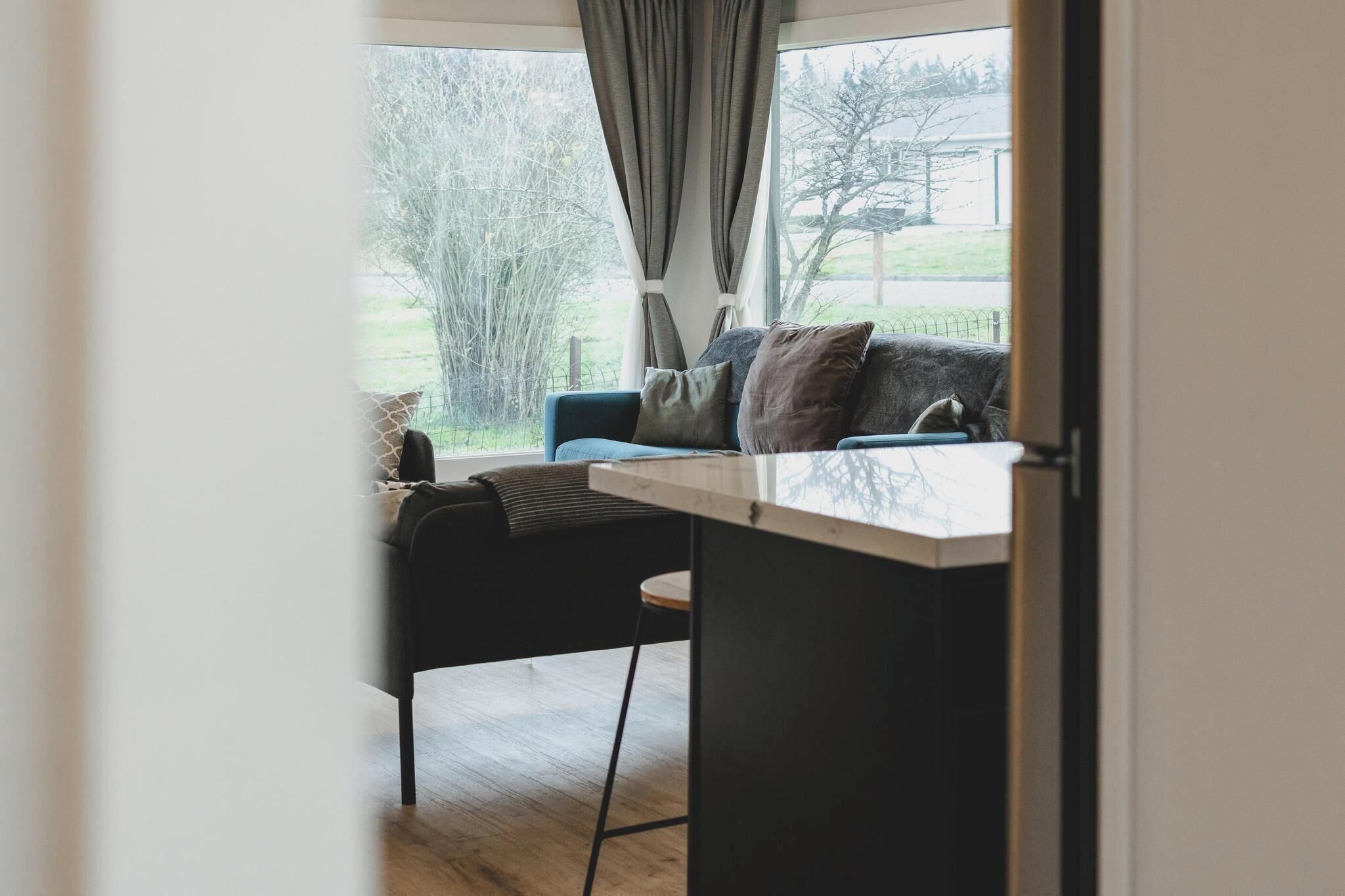 A modern living room with a sofa, a small table, and a view of a garden through a window.