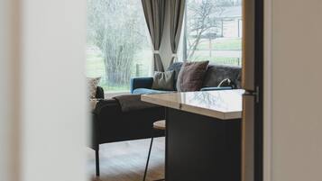 A modern living room with a sofa, a small table, and a view of a garden through a window.