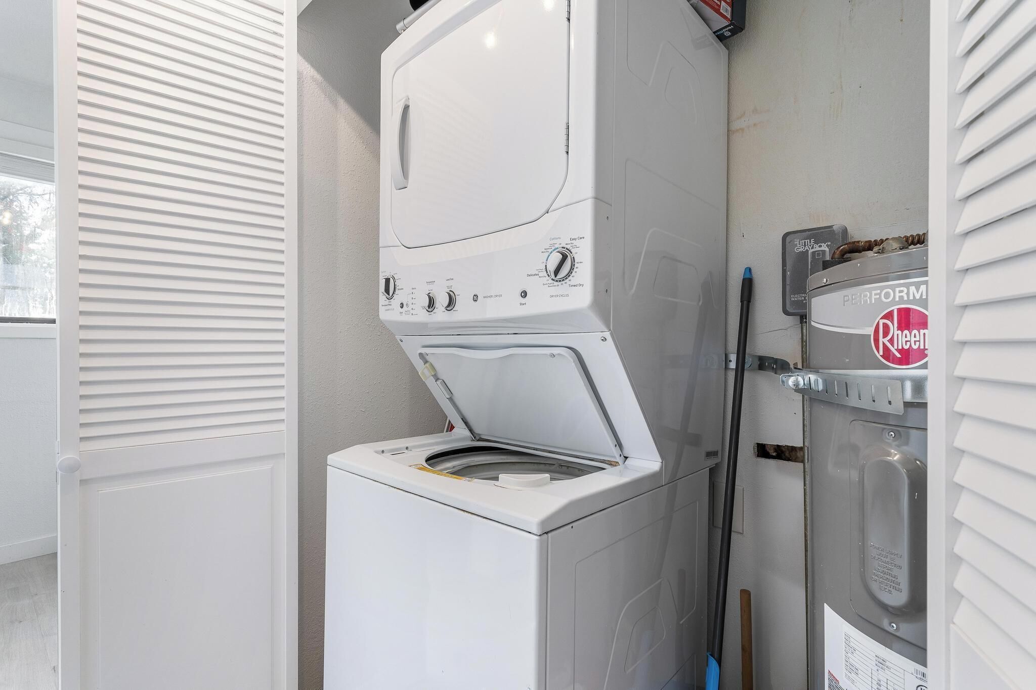 A compact washer and dryer unit with a control panel, located in a small laundry room with a window and blinds.