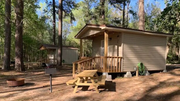 Une cabane en bois avec une véranda et une table de pique-nique, située dans une zone boisée.
