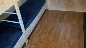 Une chambre avec un lit superposé, des murs en bois, une fenêtre avec des stores et un luminaire au plafond.