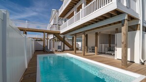 Zona de piscina con cubierta de madera, barandillas blancas y una piscina azul cristalina.