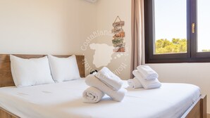 A neatly made bed with white linens and towels, a wooden headboard, a wall decoration with motivational phrases, and a window with a view of trees. - CostaBlancaDreams - Casa Leo in Benissa Costa (Benissa)