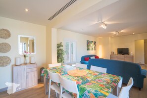 Una sala de estar moderna con comedor, un sofá azul, un televisor y un mueble aparador.