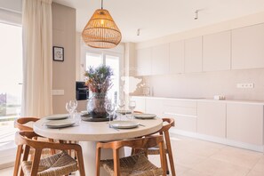 Enjoy meals in this dining area with a round table for four, a wicker chair, and a vase of flowers.