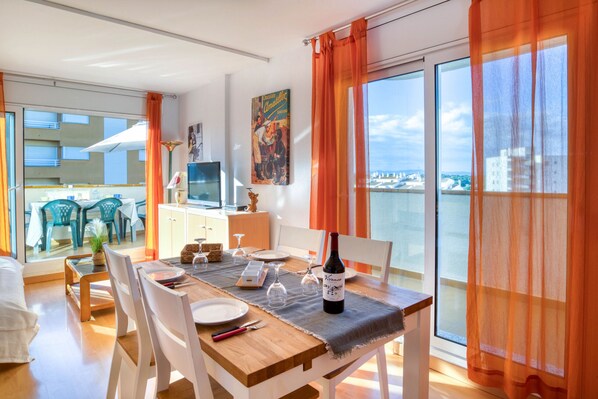 Un coin repas avec une table dressée pour deux personnes, une bouteille de vin et une vue sur la ville grâce à de grandes fenêtres.