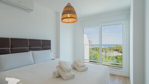 Un dormitorio con una cama grande, dos toallas blancas, una lámpara colgante y una ventana con vistas a la ciudad.