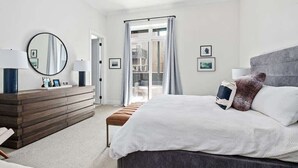 Une chambre à coucher moderne, dotée d’un grand lit, d’une commode, d’un miroir et offrant une vue sur l’extérieur par une fenêtre.