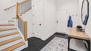 Un escalier avec des marches en bois et des rampes noires, une porte blanche, une petite table avec un bol, et un miroir accroché au mur.