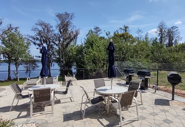 An outdoor patio with tables and chairs, a grill, and a view of the lake.