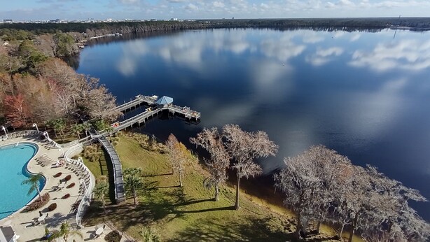 A lakeside resort with a swimming pool, a dock, and a bridge connecting to the water.