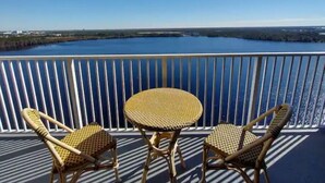 A balcony with a round table and two wicker chairs, overlooking a large body of water.