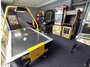 A room with a ping pong table, arcade games, and a vending machine.