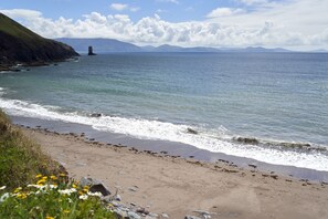 A beach with a rocky shoreline, waves, and a distant lighthouse.