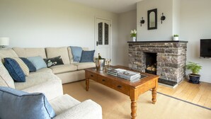 Un salon avec un canapé beige, une table basse en bois, une cheminée en pierre et un téléviseur fixé au mur.