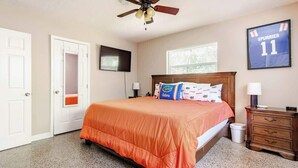 Une chambre à coucher avec un lit, un ventilateur de plafond, une table de chevet, un maillot encadré et une fenêtre.