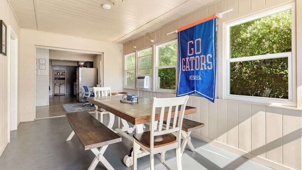 Un coin repas avec une table et des chaises en bois, une cuisine à l’arrière-plan et une banderole sur le mur avec l’inscription « ALLEZ, LES GATORS ! ».