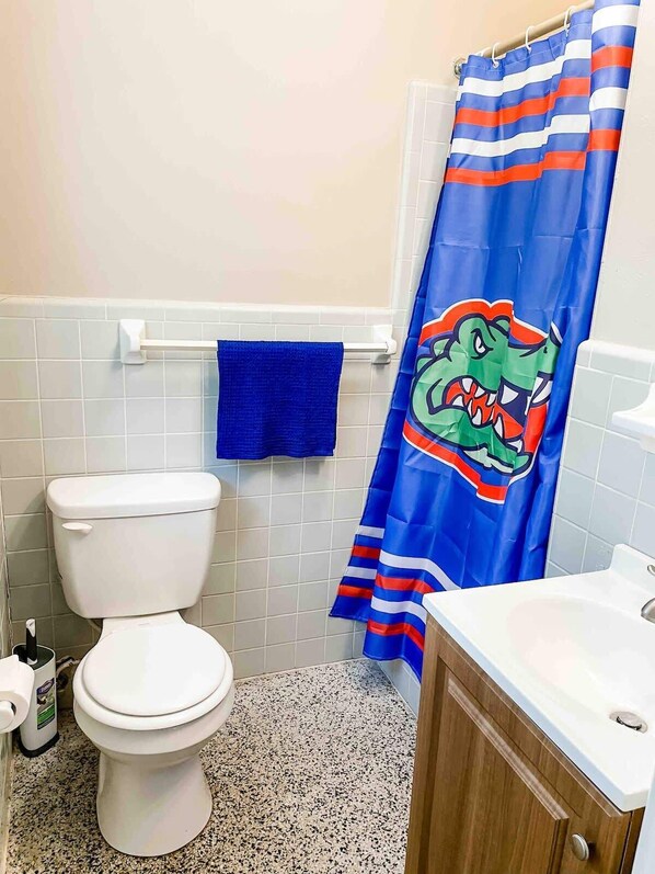 Un baño con un inodoro blanco, una toalla azul y una cortina de ducha rayada con diseño de cocodrilo.