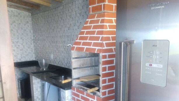 A kitchen with a brick oven, a stainless steel refrigerator, and a tiled backsplash. - Farol House (Marica)