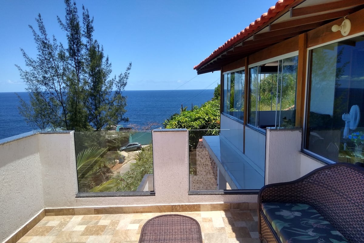 A balcony with a view of the sea, a wicker table, and a sofa.