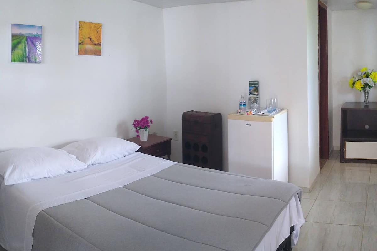 A hotel room with a large bed, a small desk, a chair, a nightstand, and two wall-mounted paintings.