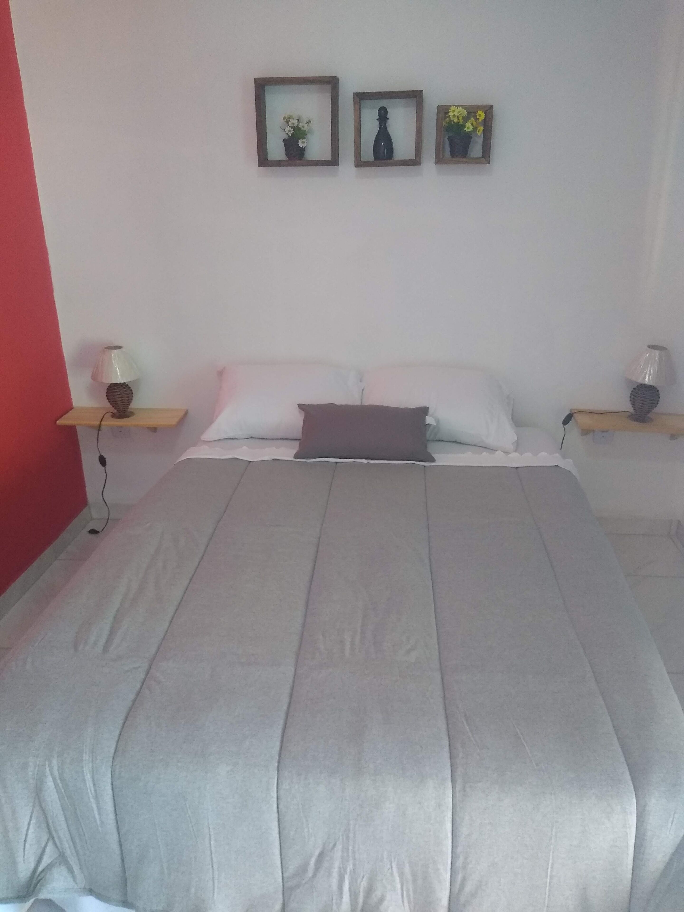 Une chambre à coucher avec un grand lit, deux tables de chevet avec des lampes et trois tableaux encadrés accrochés au mur.