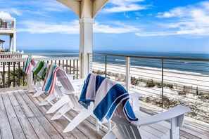 A wooden deck with white lounge chairs, each with a towel. A beach and ocean are visible in the background.