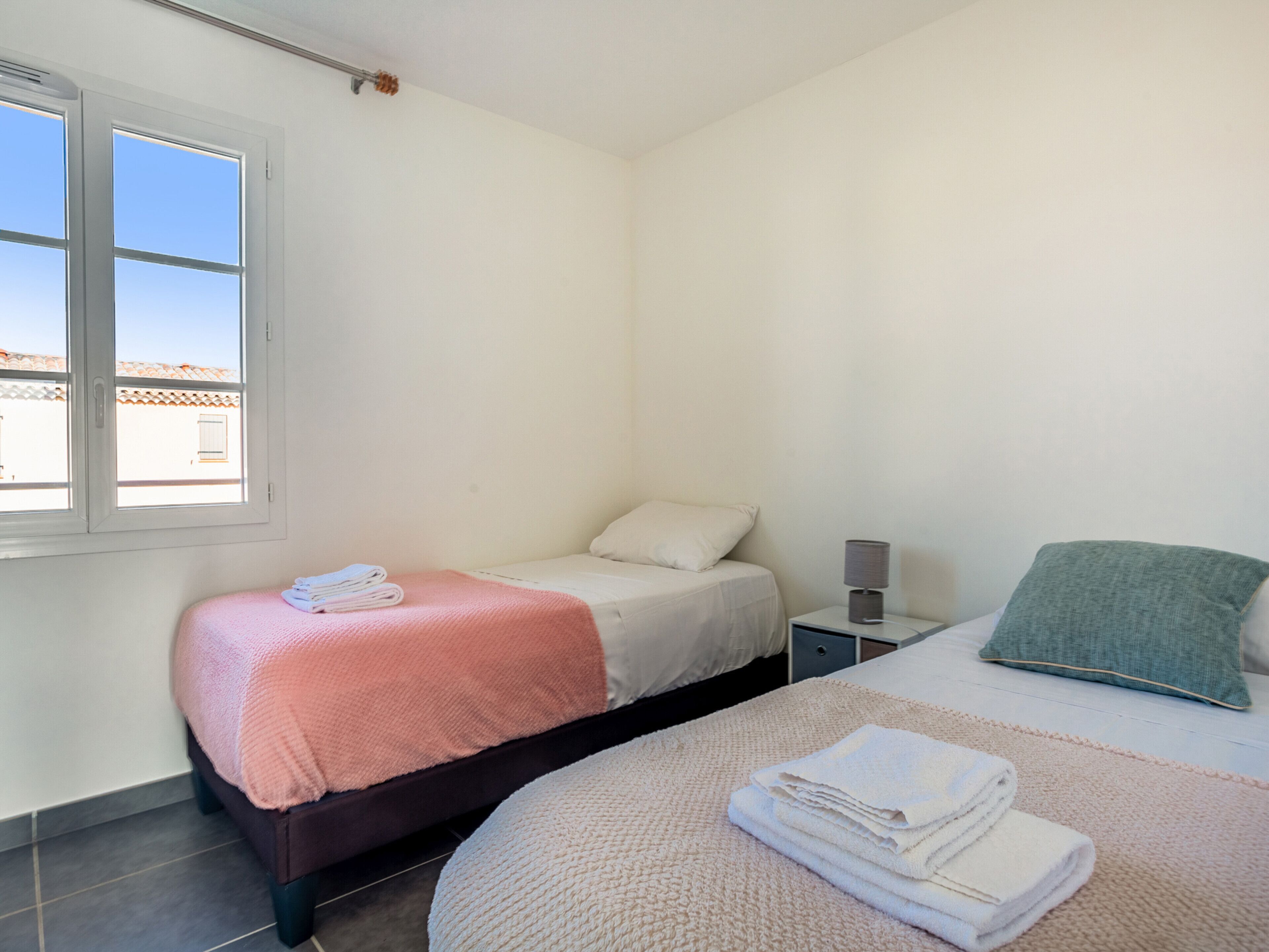 A bedroom with a bed, a bedside table, a lamp, and a window.