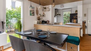 A modern kitchen with a wooden island, a dining area with a dark table and grey chairs, and a view of greenery outside. - Maison Erable - Welkeys (Lyon)