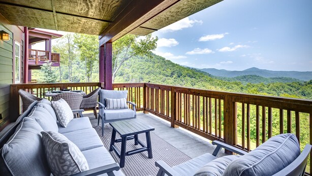A covered outdoor seating area with a wooden deck, a sofa, and a table. - Escape the Heat in the High Country - 3 King Bedrooms & Amazing Views! (Banner Elk)
