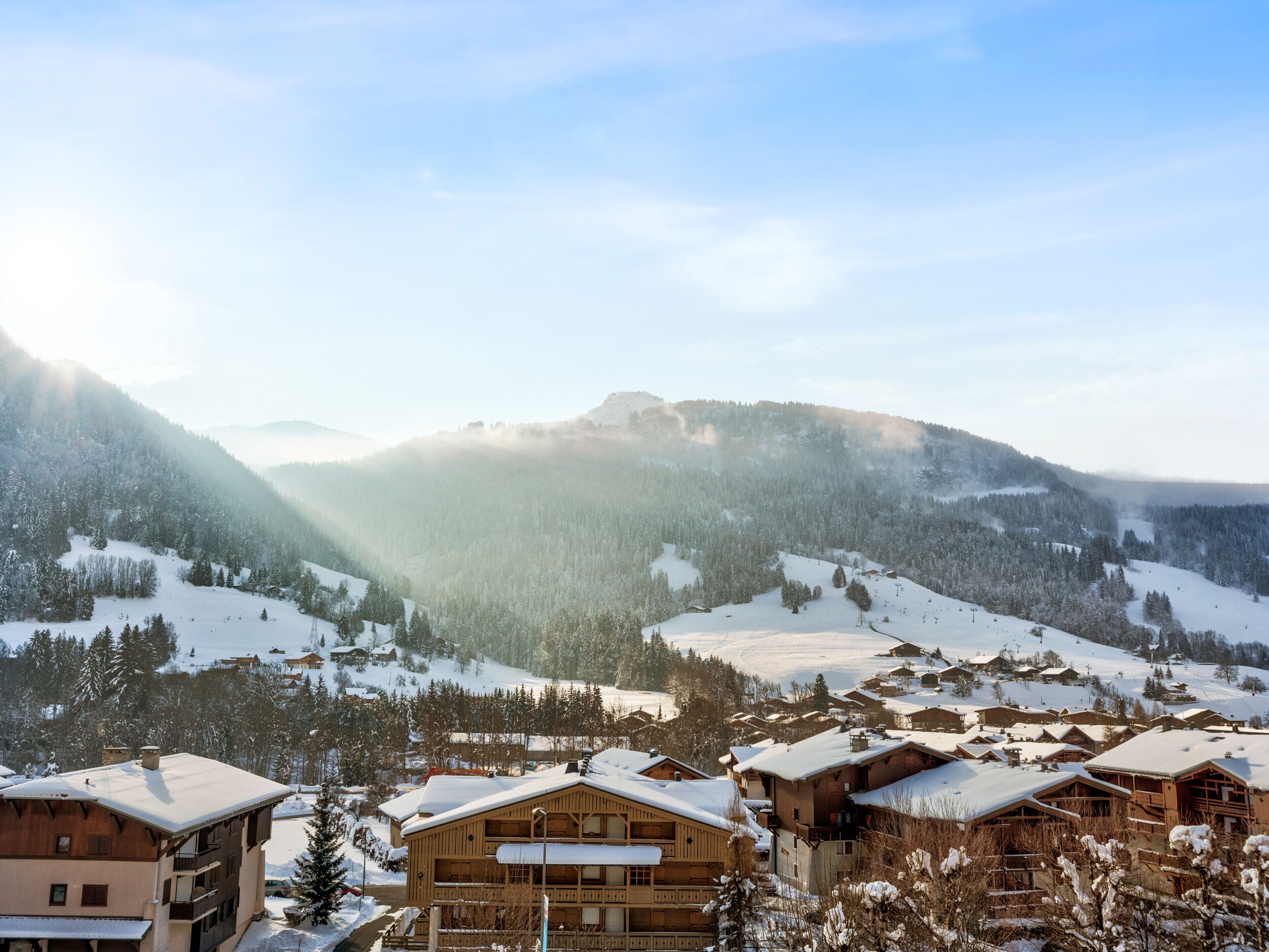 A mountain resort with wooden buildings, snow-covered slopes, and a clear sky.