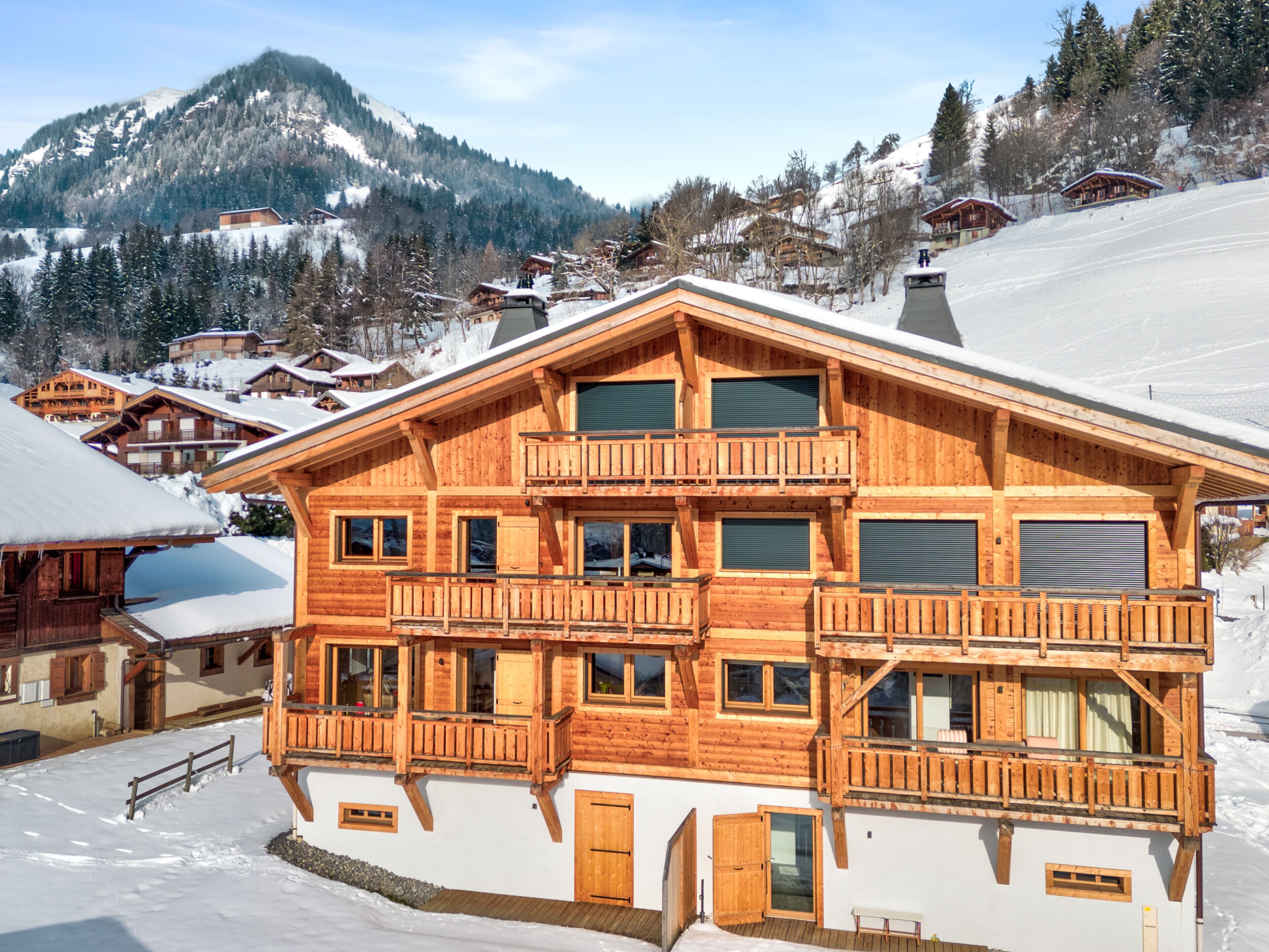 Una baita in legno con diversi balconi, ampie finestre e montagne sullo sfondo.