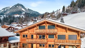 A wooden chalet with multiple balconies, large windows, and a mountain backdrop. - Duplex Aravis - Welkeys (Praz-sur-Arly)