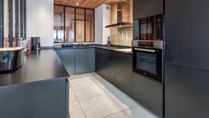 A modern kitchen with a wooden ceiling, large windows, and a built-in oven. - Duplex Aravis - Welkeys (Praz-sur-Arly)