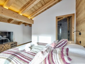 Een slaapkamer met een houten plafond, een groot bed met gestreepte beddengoed, een televisie op een houten kast en een nachtkastje met een lamp.