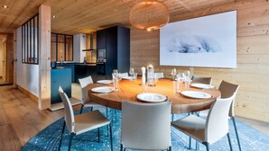 A modern dining room with a wooden ceiling, a round table set for six, and a large painting on the wall. - Duplex Aravis - Welkeys (Praz-sur-Arly)