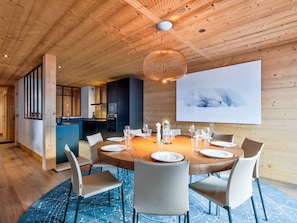 Un comedor moderno con techo de madera, una mesa redonda para seis personas y un cuadro grande en la pared.