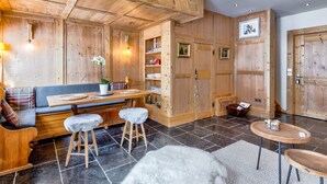 A wooden interior with a sofa, stools, a table, and a rug. - La Suite Darray - Welkeys (Megève)